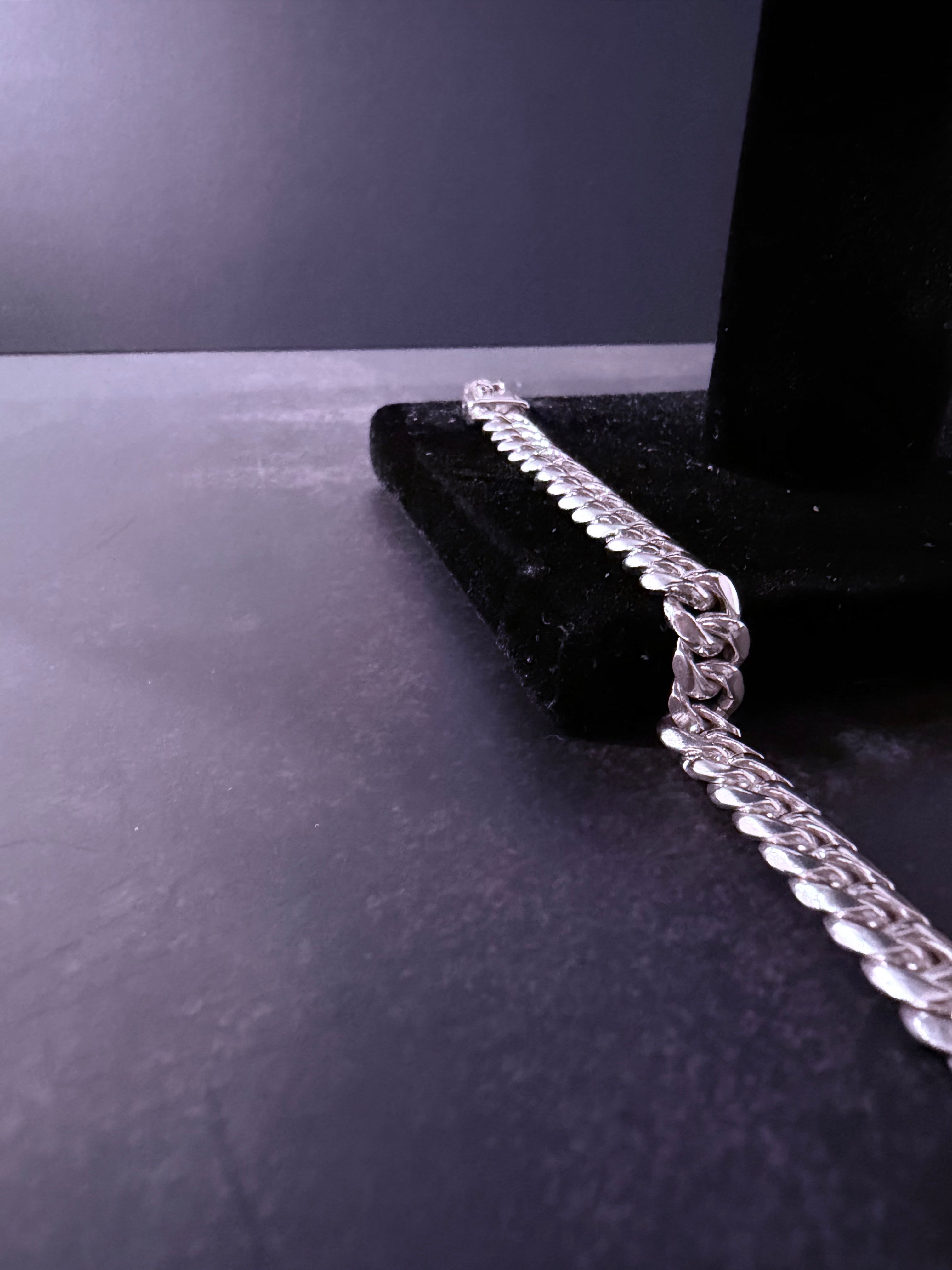 A silver-toned curb chain necklace draped over a black velvet jewelry display stand on a dark gray surface.