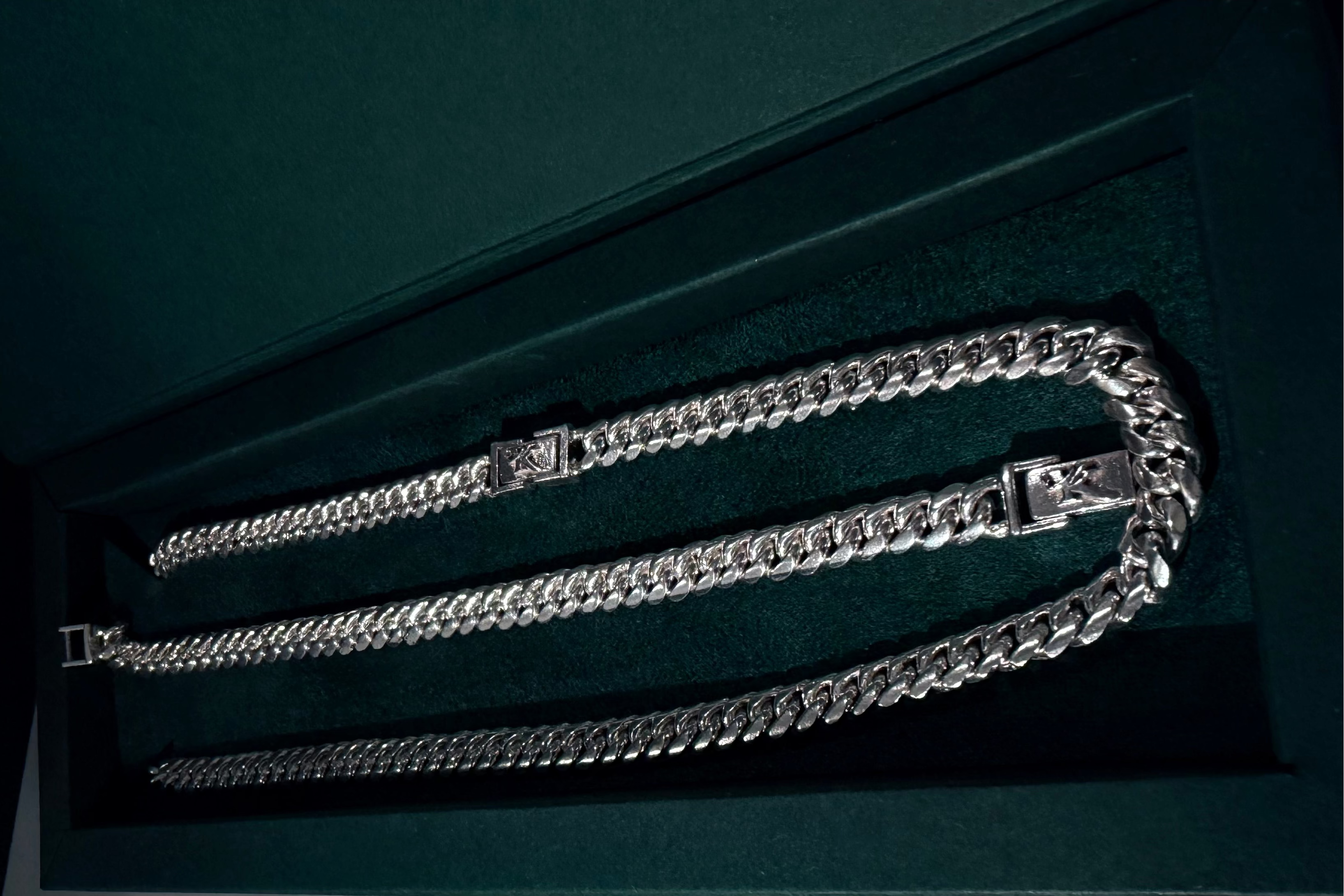 Translation missing: en.A silver-toned Cuban link chain necklace displayed inside a dark green presentation box with a velvet-like interior