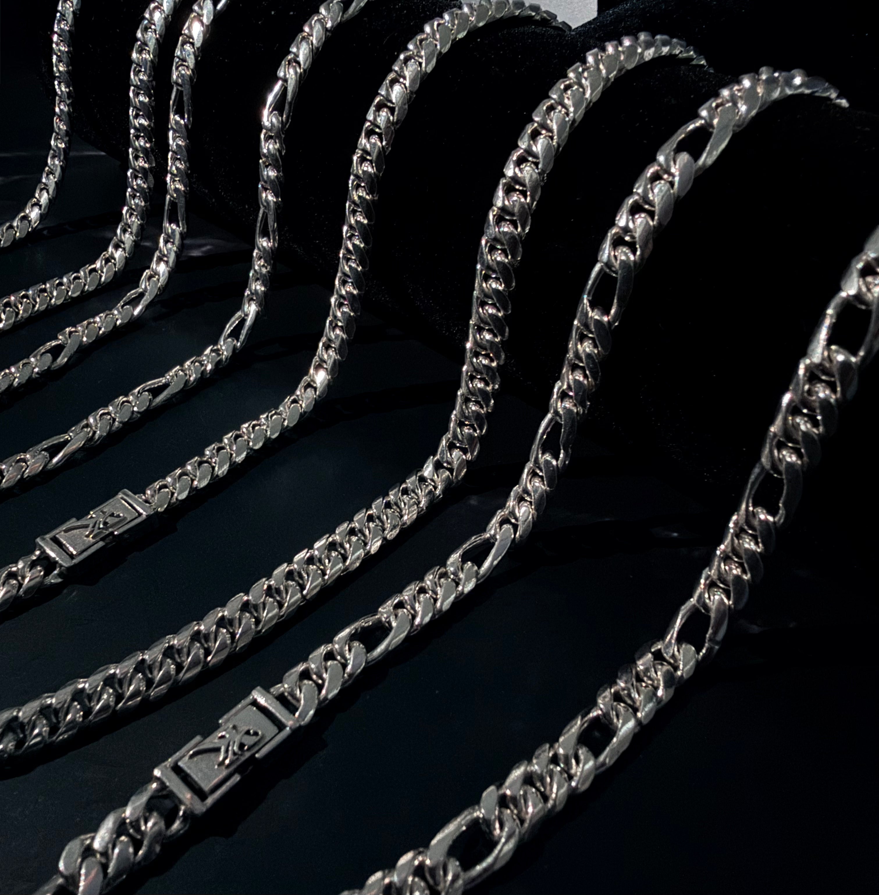 Translation missing: en.A close-up of several silver-toned metal chains arranged in curved lines on a dark textured background