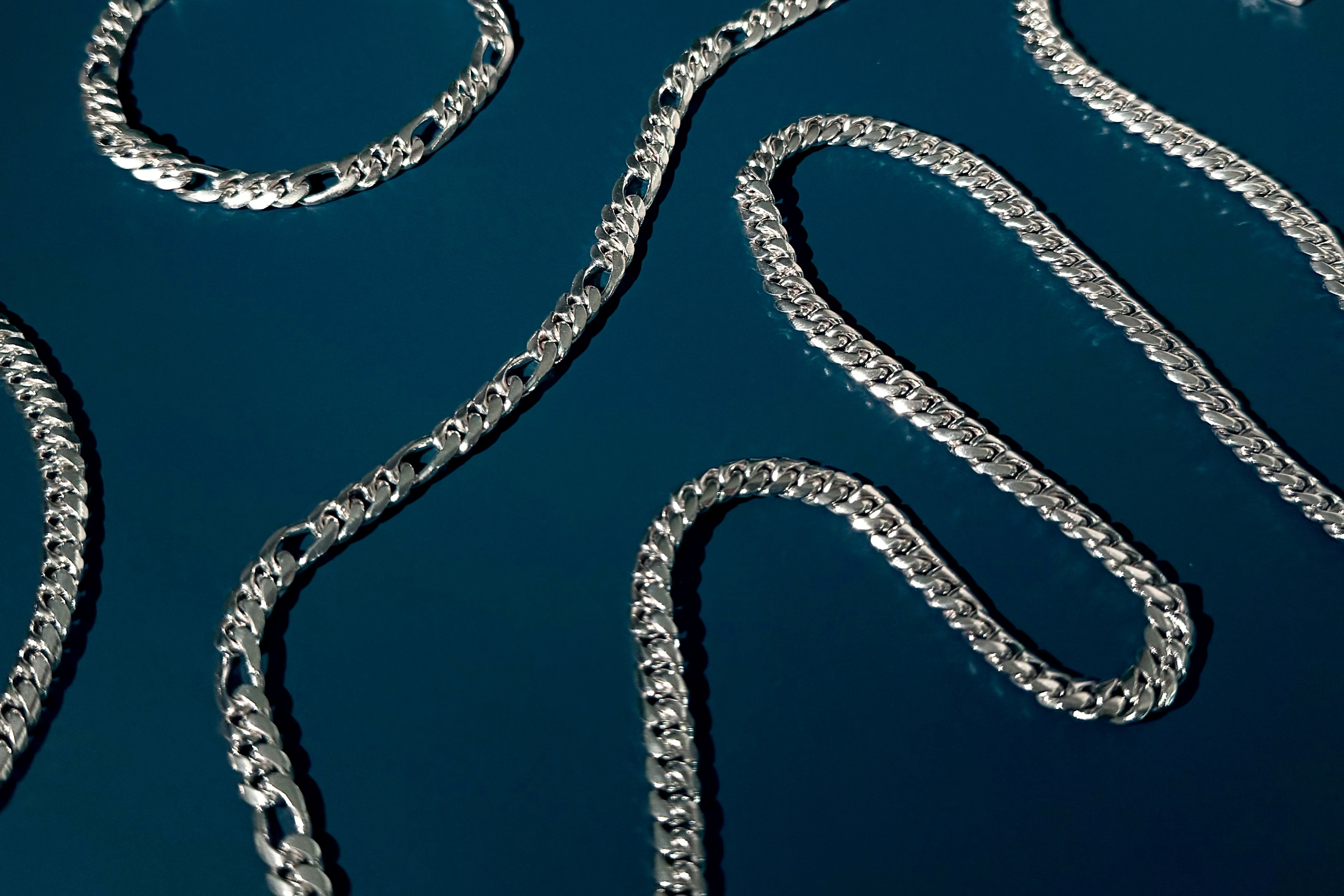 Silver-tone chain necklaces and bracelets arranged on a dark blue reflective surface.