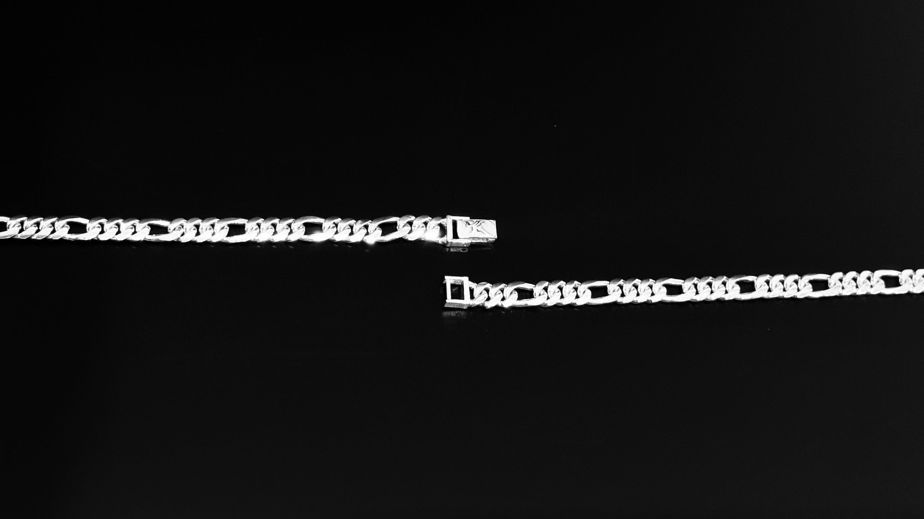 A silver-toned metal chain bracelet with rectangular links, shown in two close-up segments against a solid black background.